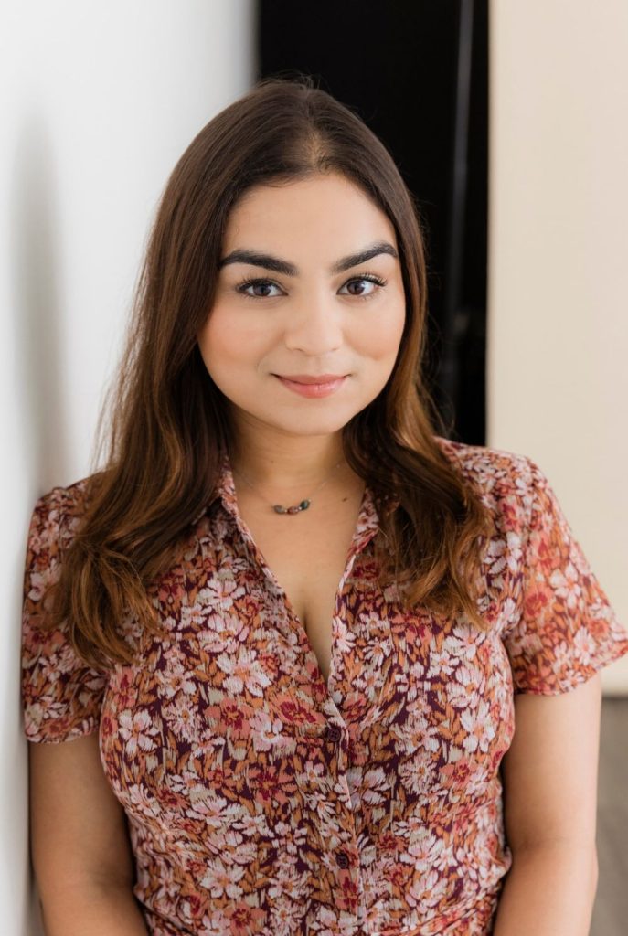 A young woman with long brown hair wearing a floral print blouse.