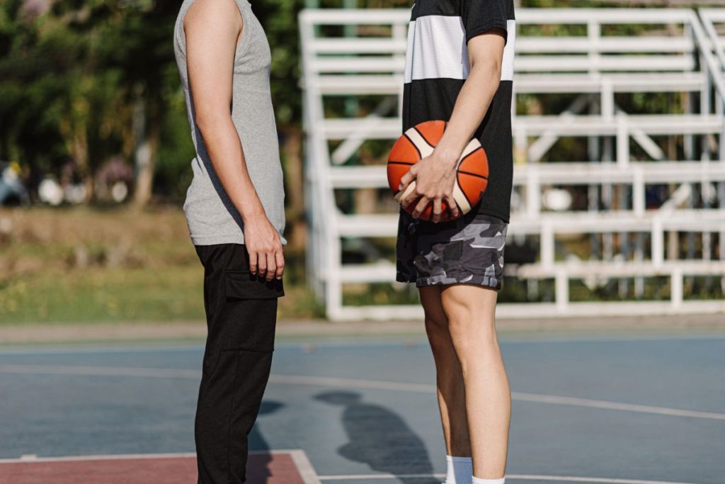 Two basketball players stand facing each other on an outdoor court, one holding the ball — sport psychologist work centers on the one-on-one relationship between practitioner and athlete, building mental skills through structured practice